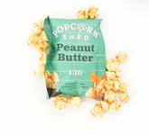 Green 'Popcorn Shed' peanut butter popcorn bag with popcorn around it on a white background